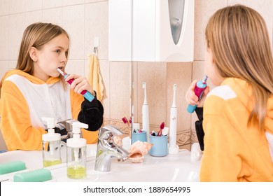 Tween Girl Wearing Orange Pyjamas Brushes Her Teeth With Electric Toothbrush In A Bathroom