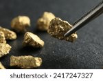 Tweezer with shiny gold nugget over grey surface, closeup. Space for text