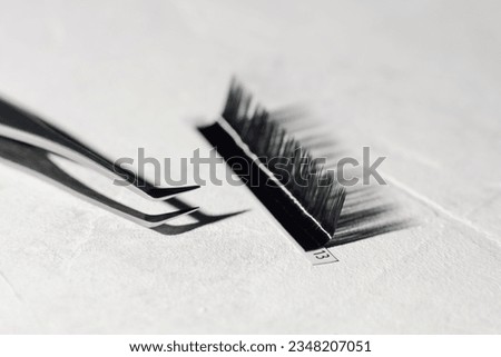 Tweezers with sharp tip, using for isolating small lashes, lying near palette of black artificial eyelashes on white table with cast shandows of tools. Instruments for cilia extension procedure.