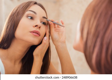 Tweezing Eyebrows. Beautiful Young Woman Tweezing Her Eyebrows While Looking At The Mirror