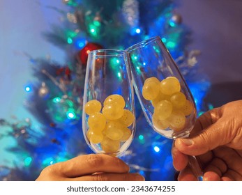Twelve grapes in the glasses in hands. Selective focus, Christmas tree background. Traditional Spanish to eat twelve berries for good luck at midnight. New Year's Eve.