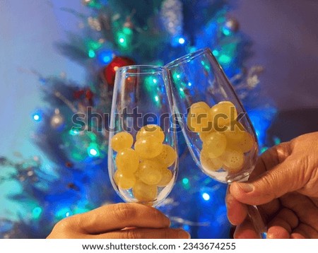 Twelve grapes in the glasses in hands. Selective focus, Christmas tree background. Traditional Spanish to eat twelve berries for good luck at midnight. New Year's Eve.