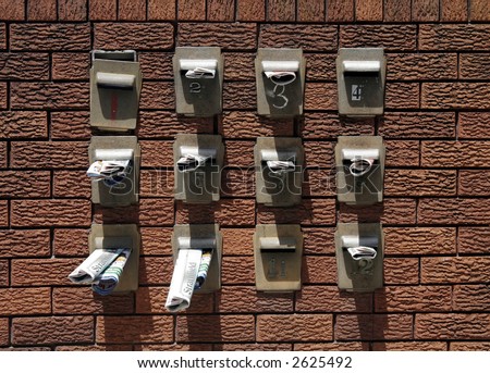 Twelve Mailboxes With Newspapers Inside On A Red Brick Wall