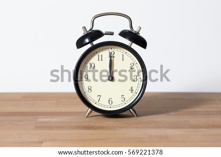 It is twelve o'clock. The time is 12:00 am or pm and noon or midnight. A retro clock isolated on wooden table. White background. Copy space and cut.