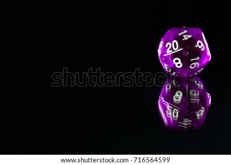 A twenty sided  polyhedral die on a mirrored surface. These type of dice are used for role playing games.