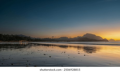 Twilight after sunset on a tropical island. The blue sky is highlighted with orange at the horizon. Silhouettes of mountains. Ocean waves are spreading over the beach. Reflection on wet sand. Lights - Powered by Shutterstock