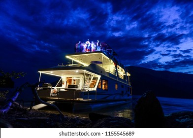 Twilight Houseboat Dance Party Featuring A  Night Sunset Sky, Lake, Beach And Boat. This Horizontal, Long Exposure Shot Was Taken With A Low Angle View Looking Up On Shuswap Lake In British Columbia. 