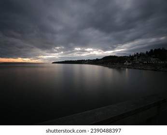 Twilight over calm waters with a dramatic cloudy sky and coastal town silhouette.