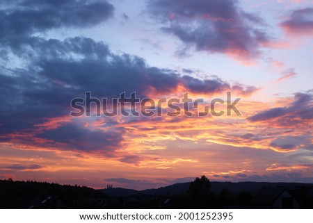 Twilight sky after sunset, clouds in red, orange ,blue, violet, purple, crimson colors. Silhouettes of houses roofs, trees, monastery on the hill and forest.  Colorful scenery skyline background.