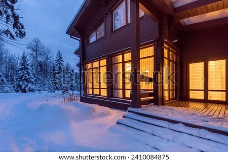 It's twilight time. Bright light from the windows of a private wooden house against a snowy landscape.