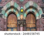 Twin arched wooden doors with decorative stonework and antique hanging lantern at United Parish in Brookline, Massachusetts, USA