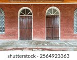 Twin arched wooden doors with iron hardware, framed by red brick wall, in a peaceful architectural setting