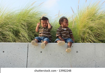 Twin Babies Sitting On A Ledge.