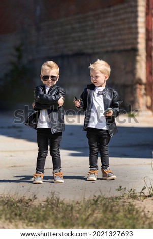 Twin brothers in leather jackets and sunglasses.Two identical blond boys against the abandoned building.Children in a cool and bold image for a photo shoot.Children look like celebrities or models.