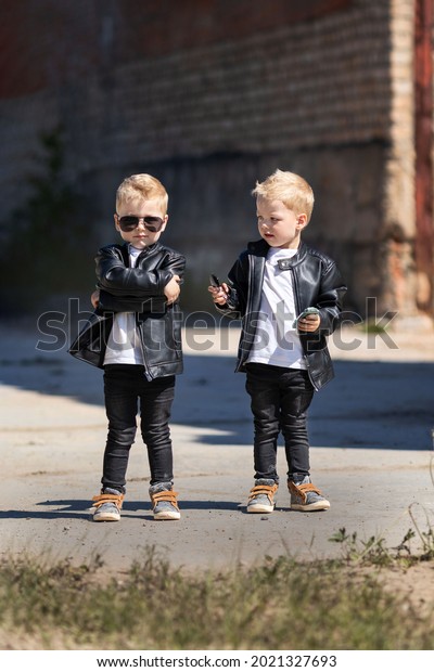 Twin brothers in leather jackets and\
sunglasses.Two identical blond boys against the abandoned\
building.Children in a cool and bold image for a photo\
shoot.Children look like celebrities or\
models.