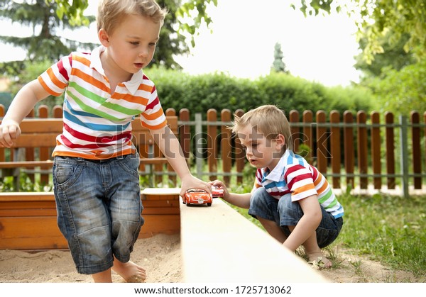 Twin brothers\
playing in sandpit with toy\
cars