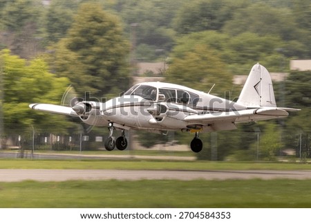 Twin engine landing, light multi engine aircraft moments before touch down. Landing gear is deployed and throttles at idle in the flare. Red and white general aviation airplane approaching
