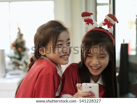 Twin girls with long hair wearing a red tease each other happily.