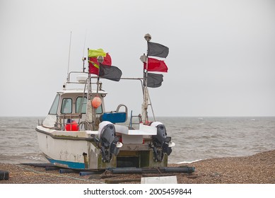 Twin Outboard Motor Glass Fibre Hull Fishing Boat In Aldeburgh Suffolk England UK Flying Red Black Yellow Flags, Sitting On Stone Beach, Facing Sea, No People, Grey Sky, Strong East Wind Blowing.