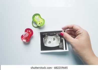 Twin Pregnancy. Two Soothers,an Ultrasound Picture Of Two Babies And A Mother's Hand.