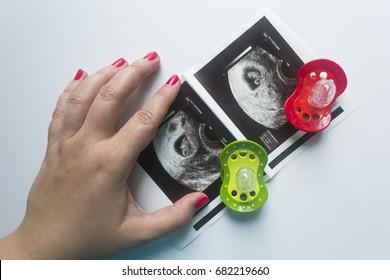 Twin Pregnancy. Two Soothers,an Ultrasound Picture Of Two Babies And A Mother's Hand.