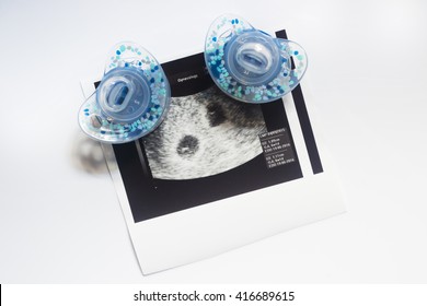 Twin Pregnancy Ultrasound. Two Soothers And An Ultrasound Picture Of Two Babies.