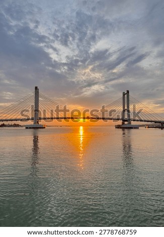 Twin Pylon Cable Stayed Bridge Over Sea at Sunset with Perfect Water Reflection
Wide view of a modern cable stayed bridge with two tall pylons spanning over calm sea during golden sunset. Symmetrical composition with sun positioned between pylons and perfect reflection on water surface.