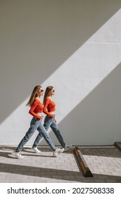 The Twin Sisters Stepping Forward In Sync. Diagonal Shadow Of Natural Sunlight, Urban Area.