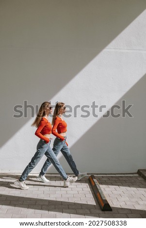 The twin sisters stepping forward in sync. Diagonal shadow of natural sunlight, urban area.