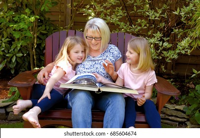 Twin sisters take time out for a story
time with grandma. They sit together 
in a wooden lawn chair listening to a
story told to them by their grandparent.