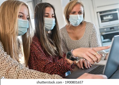 Twin Sisters And Their Teacher Wearing Protective Mask And Working Their Lesson  On  A Laptop At Home During Lockdown Due To Covid-19