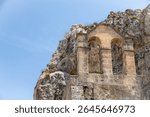 Twin-arched stone bell gable built into the rocky cliffside, photographed in Matera, Basilicata, under a bright and cloudless blue sky.