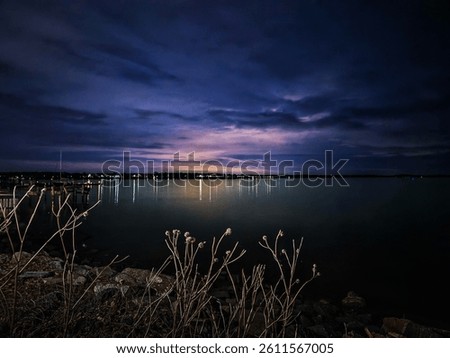 Twinkling lights dance on the water’s surface in Havre de Grace, casting a serene glow across the quiet, scenic waterfront at dusk.