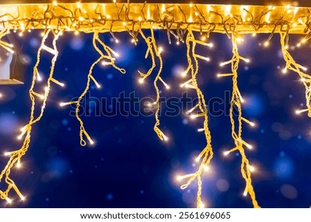 Twinkling string lights hang from a surface, casting a warm glow against a rich blue background during a cozy winter evening gathering.