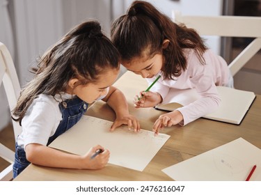 Twins, children and together for education, homework and development by studying and learning at home. Girl, students and pencil as sisters for teamwork, growth or help with books or sketch at table - Powered by Shutterstock