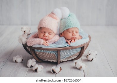 Twins are newborn brother and sister. Newborn girl and boy. Hats with white fur balls sleep sweetly in a basket.
