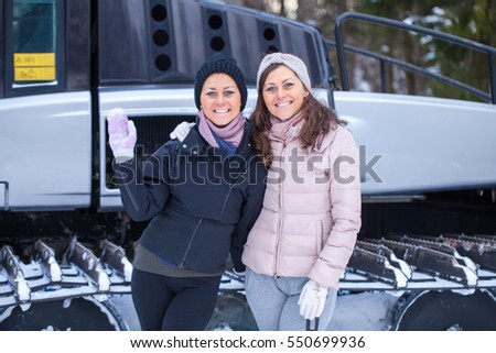 Twins posing on ski resort with snow groomer on background