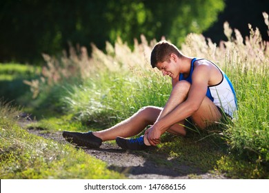 Twisted ankle. Young runner touching his sprained leg