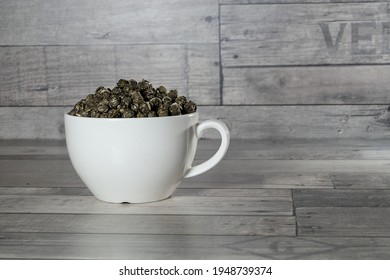 Twisted Tea Leaves In A White Cup On A Gray Wooden Background