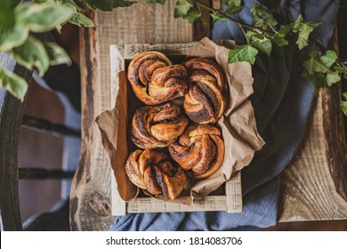Twisted traditional Swedish cinnamon rolls on wooden box, rustic table with chair and textile. The sweet homemade buns or little babka pastries. Freshly baked dessert. Top view, flat lay copy space.