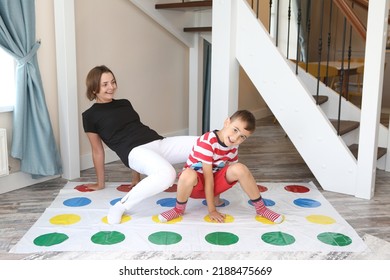 Twister game. Happy family having fun together, playing twister game at home. Mother and child, kid, boy plays in twister. Active rest, recreation, indoor game. Child with parent plays twister game