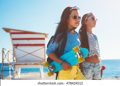Two 10 years old children wearing cool clothing posing with colorful skateboards on the beach in sunlight, urban style, pre teen summer fashion.