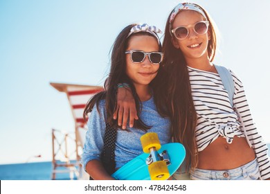 Two 10 years old children wearing cool clothing posing with colorful skateboards on the beach in sunlight, urban style, pre teen summer fashion.