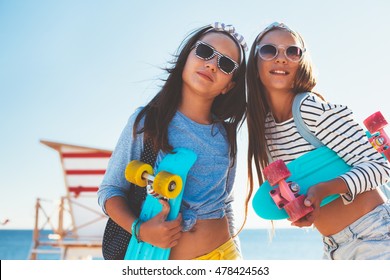 Two 10 years old children wearing cool clothing posing with colorful skateboards on the beach, urban style, pre teen summer fashion.