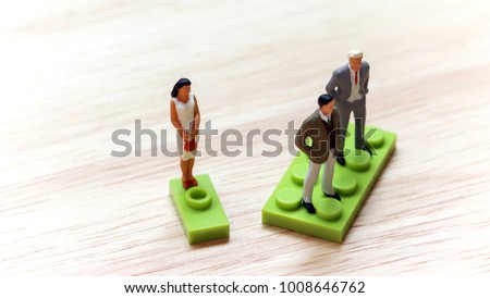 The concept of gender discrimination. Two miniature men and a miniature woman standing on a block of different size.