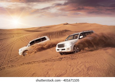two 4x4 vehicles bashing side to side through the desert dunes in the evening sun - Shutterstock ID 401671105