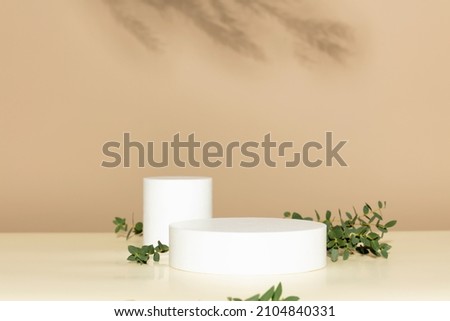 Two Abstract empty white podiums with eucalyptus leaves on beige background. Mock up stand for product presentation. 3D Render. Minimal concept. Advertising template