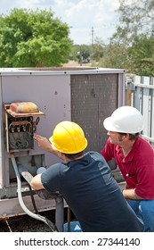 Two AC Technicians On A Roof Repairing An Industrial Compressor Unit.