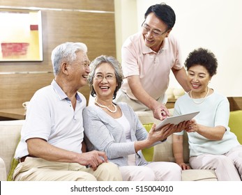 Two Active Senior Asian Couples Looking At Tablet Computer, Happy And Laughing