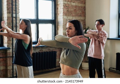 Two active teenage girls and guy crossing stretched arms in front of chest while training and repeating new movements of vogue dancing